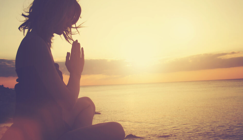 woman meditating at sunset to heal by the water